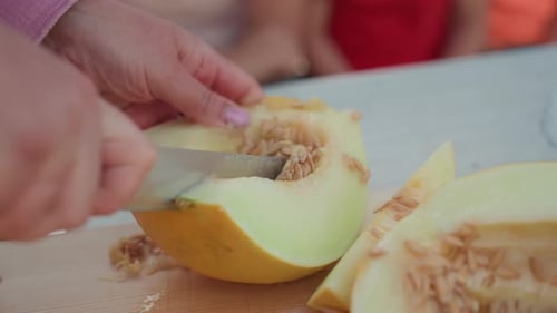 Femme caucasienne en gros plan, portionnant des quartiers de melon sur une planche en bois, été, enfants à proximité, décontractés et lumineux