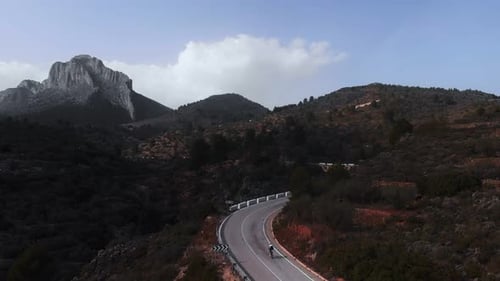 Professional strong cyclist climbing uphill on empty asphalt winding mountain road.