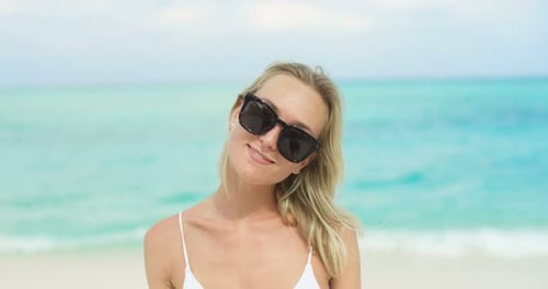 Portrait of the Beautiful Blonde Woman Wearing Sunglasses Posing and Smiling on the Beach. In the B