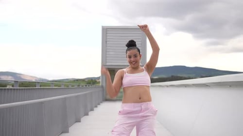 A Woman in Blue Jeans and a Blue Top is Dancing on a Bridge