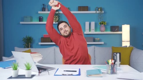 Young businessman showing how to exercise in his Home Office. He does arm exercises.