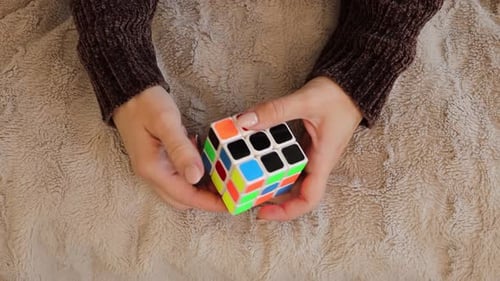 A close-up view captures a woman deeply focused on solving a colorful Rubik's Cube.