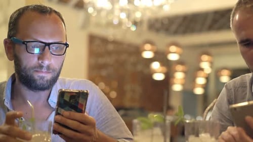 Two young men using smartphones late at night at a cafe table together