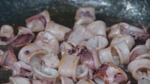 Close-up of unbreaded calamari squid tentacles frying in a pan.