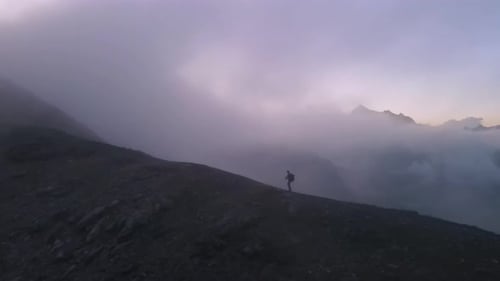Orbiting Shot of a Lone Hiker Walking along Misty foggy Mountain Peaks