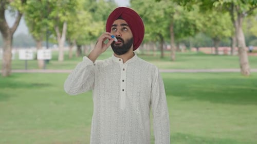 Sick Sikh Indian man measuring fever using thermometer in park
