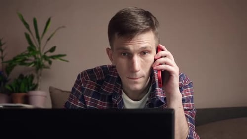Young Man Talking on Phone While Using Laptop