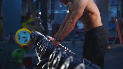 Male bodybuilder lifting heavy dumbbells at gym. Muscular man in naked torso doing workout