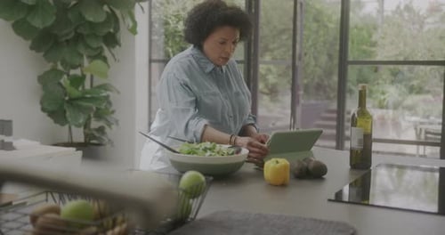 Woman Reads Tablet While Preparing Salad in Kitchen