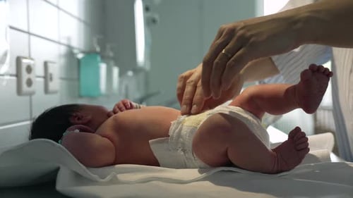Newborn baby being changed by parent on hospital bed, view of tiny legs and feet, personalized