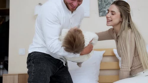 Playful family interacting on bed, father holding toddler upside-down