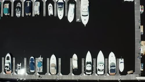 Top down aerial of boats docked in marina. Black water reflect sunshine in summer.