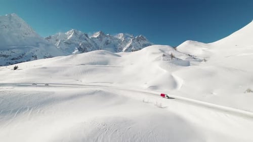 This stunning drone footage captures a small truck driving on the snowy Lautaret Pass, showcasing th