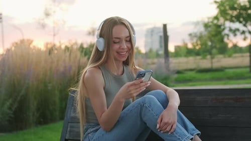Young Woman in Headphones Rests Hugging Legs on Park Bench