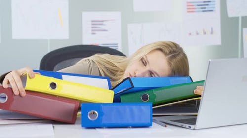 Woman Exhausted at Desk Surrounded by File Folders