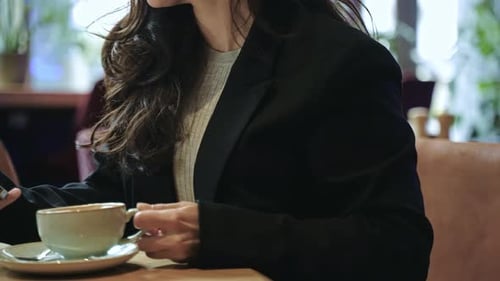 Caucasian Girl Sitting Inside of a Cafe Drinking Coffee and Typing on Her Smartphone