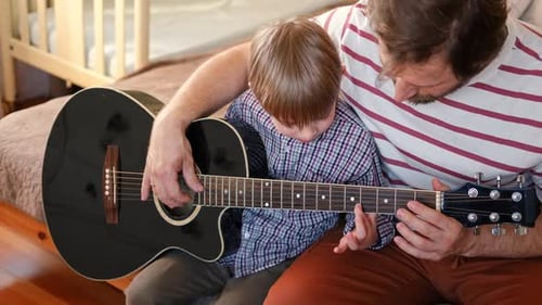 Dad Teaching Child to Play Guitar at Home