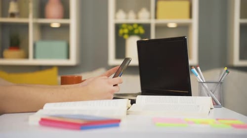 Smartphone Use with Laptop and Books on Desk