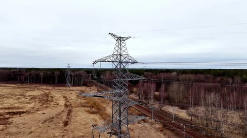 Aerial view of a high-voltage power line pylon standing in a green field, under a clear blue sky, ne