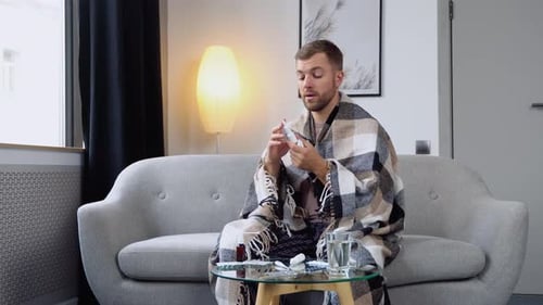 Man With Cold Using Nasal Spray on Couch