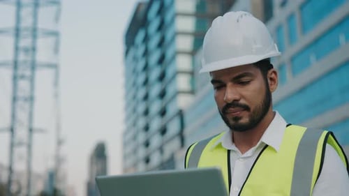 Portrait of Skilled Contractor Working on Laptop Against Modern Office Buildings