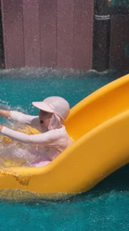 Tracking shot in slow motion of excited little girl sliding at water park on summer day