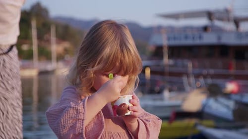 Cute Blonde Girl Eats Ice Cream on Street From a Plastic Jar