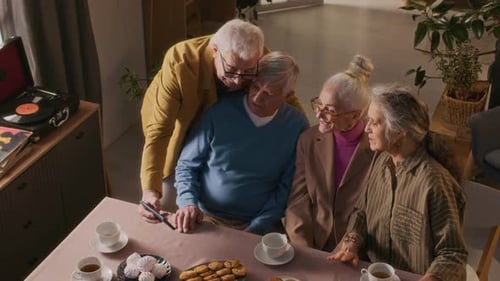 Four Senior Friends Gather Around Table Looking at Phone