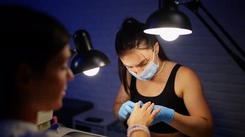 Woman Receiving Manicure from Nail Technician at Salon