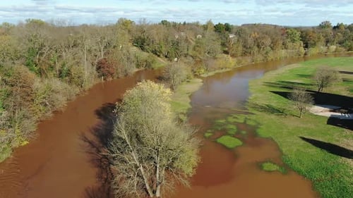 Aerial of river overflowing its banks, flood waters cover rural field, autumn trees
