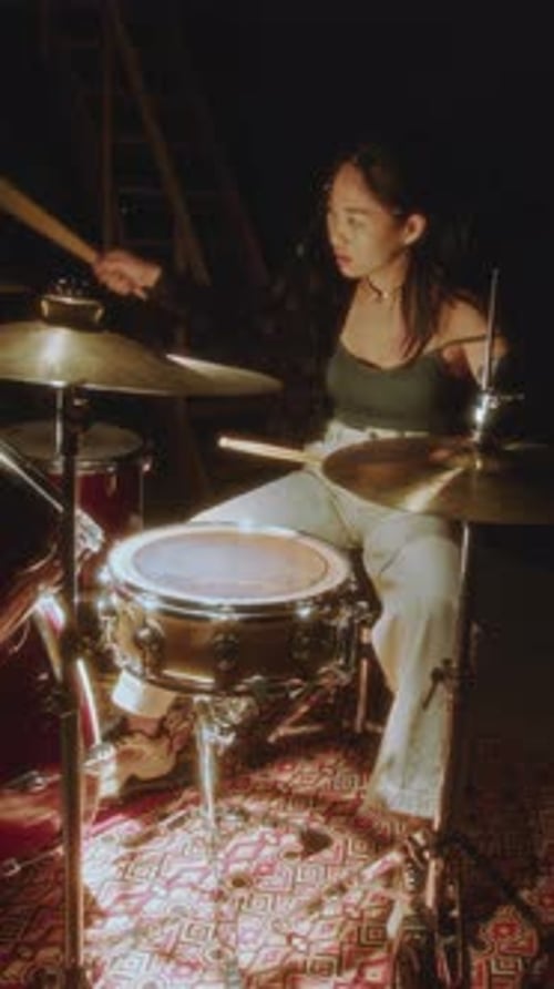 Woman Plays Drums in a Dimly Lit Room