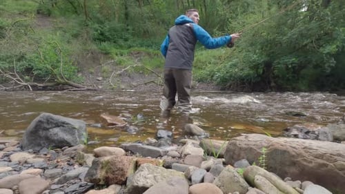 Low static shot of a man wading and fly fishing in a small secluded river in Scotland