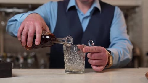 Un barman prend une carafe avec du whisky et la verse dans un verre. En gros plan