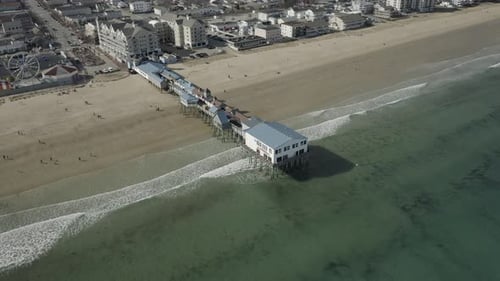 Drone shot, of a pier on the beach, flying to the right.