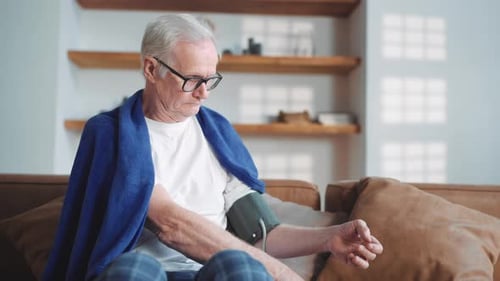 Senior Man Measures Blood Pressure on Couch