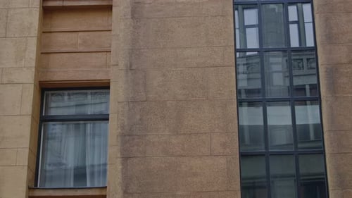 Video mit Frontansicht der Fassade eines beigefarbenen Gebäudes mit vertikal angeordneten Fenstern.