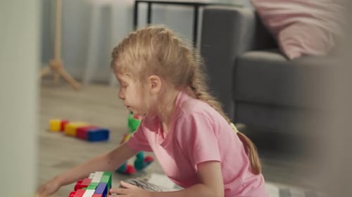 Chica rubia concentrada construye una estructura a partir de bloques de colores