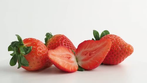 Halbierte und ganze Erdbeeren drehen sich auf weißem Hintergrund.