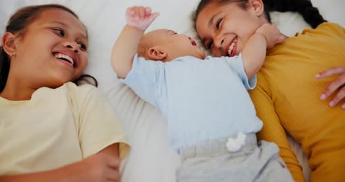 Sisters Laughing with Baby Brother on White Bed