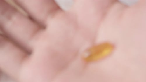 Hand showing an omega-3 fish oil capsule to the camera. Close up