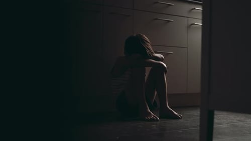 Young boy sitting on kitchen floor hugging knees and burying face in arms showing childhood
