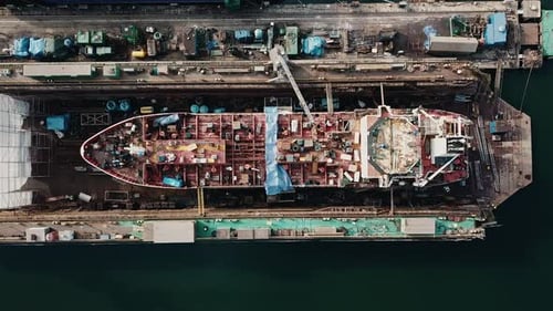 Drone flying above the big cargo ship in the shipyard docks