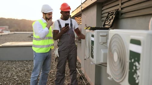 HVAC Inspection by Two Workers on Rooftop at Sunset