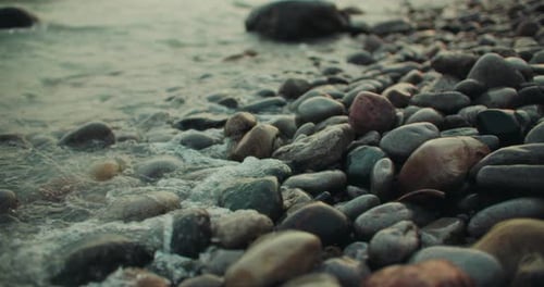 Wave Water Splashing Against Shallow Stony Beach Shore with Colorful Rocks. Coastal Rising Tide Rock