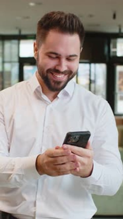 Happy Young Businessman Using Smartphone Shocked By Sudden Victory Lottery Win in Office Lobby