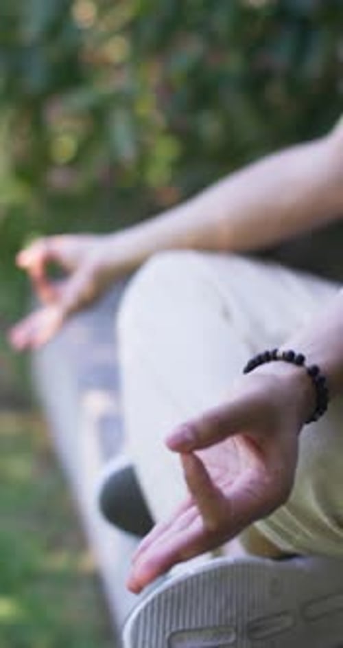 Vertical video: Man sitting on stone ledge in park, breathing, settling into mudra, copy space