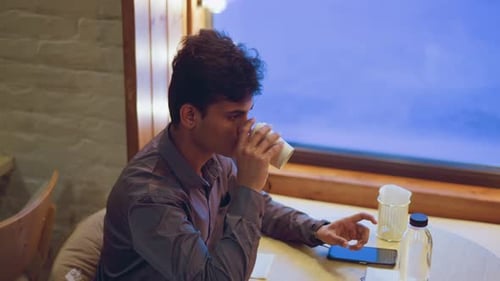Man Drinks Coffee in Cafe Next to Window