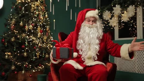 Happy Santa Claus Sits with a Gift