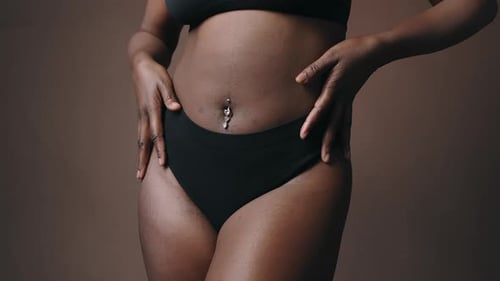 Sección media de una mujer negra en ropa interior acariciando su cuerpo