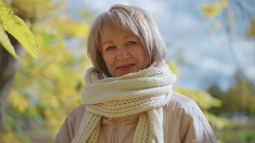 Woman with scarf stands in autumn leaves